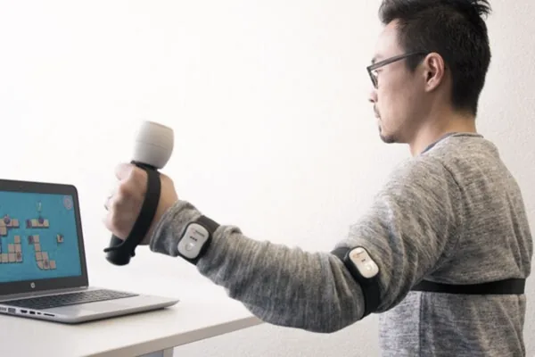 Patient trainiert den Arm mit dem ArmeoSenso vor einem Bildschirm