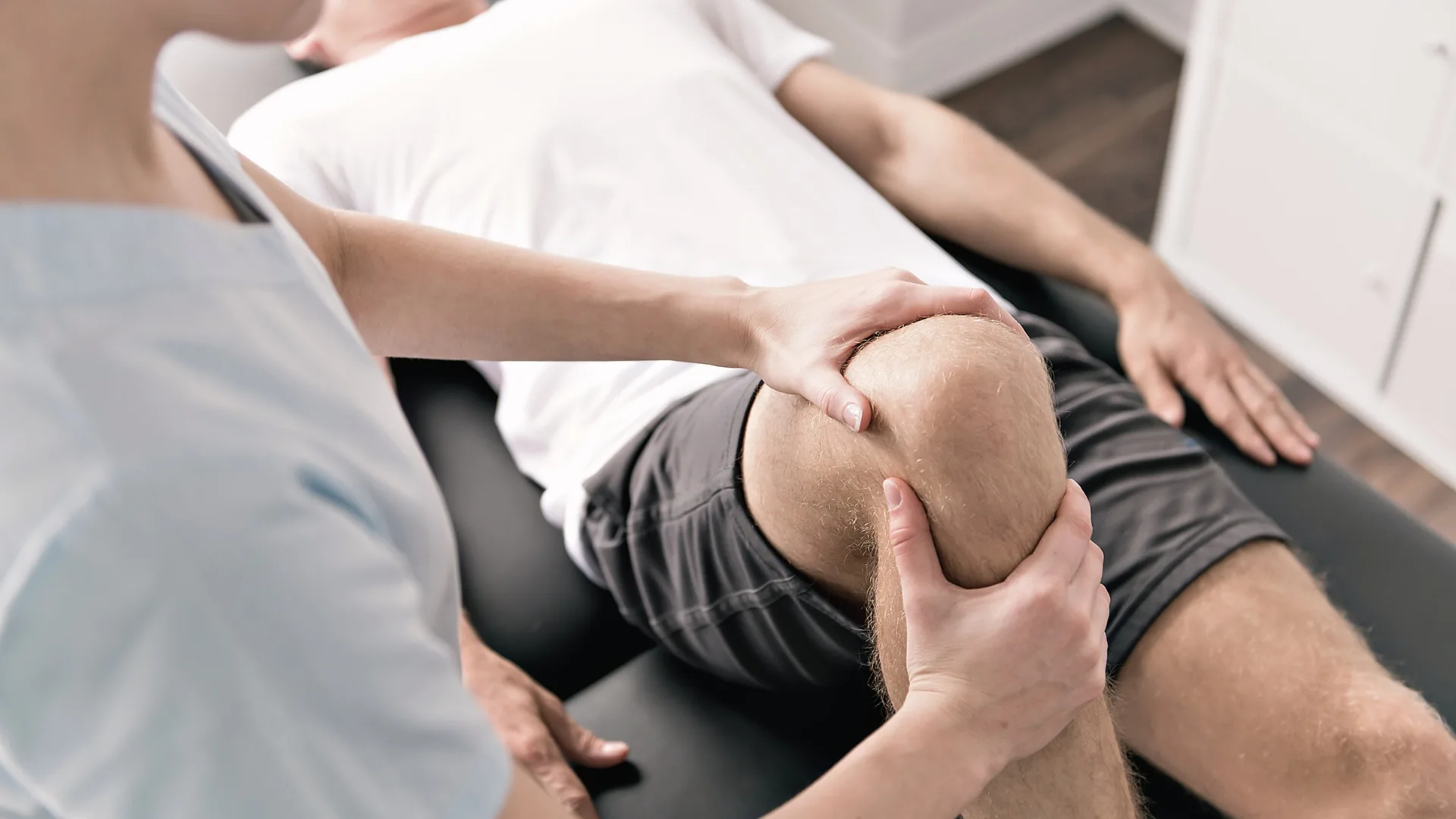 Therapeut behandelt mit beiden Händen das Knie eines Patienten auf der Behandlungsliege