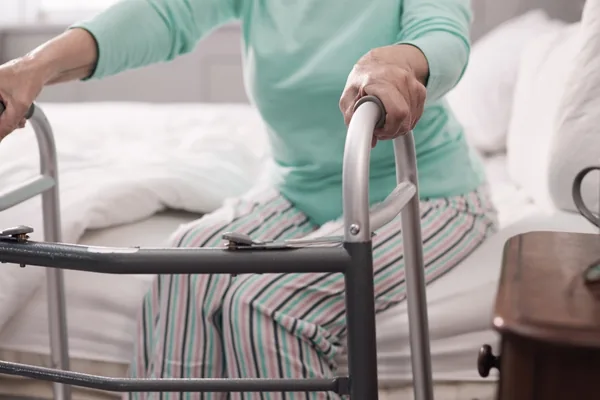 Patientin richtet sich am Gehgestell vom Bett auf